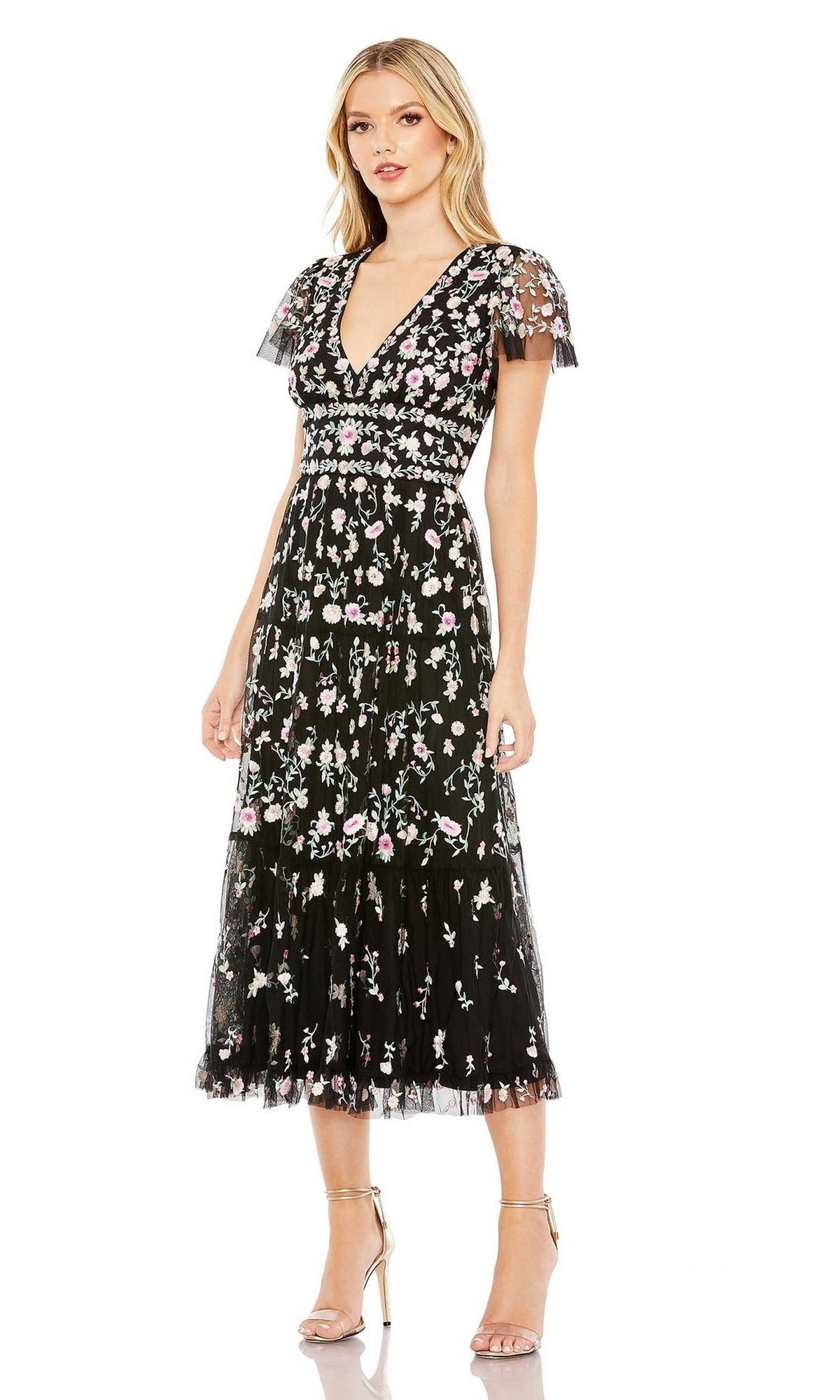 A woman wearing the Mac Duggal 35104 Embroidered Wedding-Guest Dress with pink and white floral embroidery, short flutter sleeves, v-neckline, and strappy heels stands against a white background.